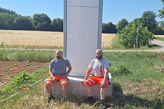 Dieses Bild zeigt wie den Pylon mit neuem Logo und 2 Mitarbeiter davor 