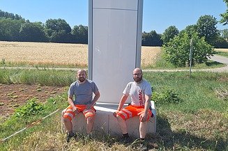 Dieses Bild zeigt wie den Pylon mit neuem Logo und 2 Mitarbeiter davor 