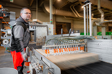 Bild zeigt einen Mitarbeiter der am fLIE?BAND ARBEITET UND EINE pLATTE WELCHE GERADE VERKLEBT WIRD